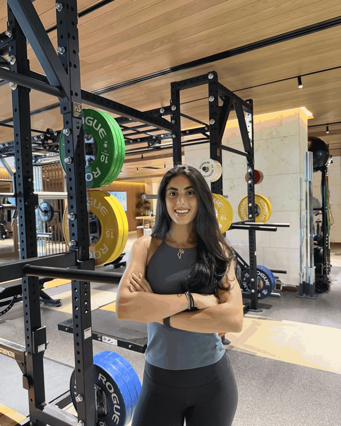Julia Charaf on the gym floor, arms crossed in front of a Rogue rack